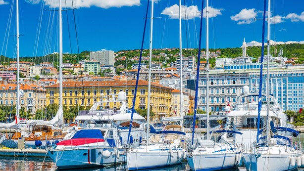 A marina with multiple sailboats docked, a cityscape with buildings in the background, and a clear blue sky. - Nurli Apt Near Glavanovo Beach (Rijeka)