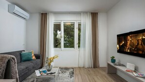 A modern living room with a grey sofa, a coffee table, a TV, and a window with curtains. - Nurli Apt Near Glavanovo Beach (Rijeka)