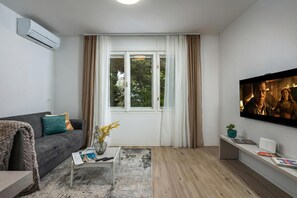 En moderne stue med en grå sofa, et sofabord, et fjernsyn og et vindue med gardiner.