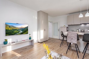 A modern kitchen with a dining area, a TV mounted on the wall, and a wooden floor. - Nurli Apt Near Glavanovo Beach (Rijeka)