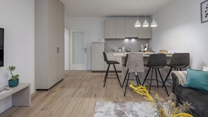 A modern kitchen with white cabinets, a dining area with four chairs, and a grey sofa with a teal pillow. - Nurli Apt Near Glavanovo Beach (Rijeka)