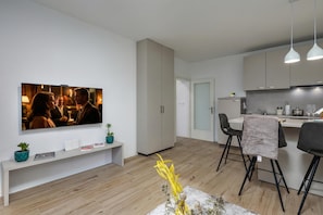 A modern kitchen with a dining area, a TV mounted on the wall, and a bench with decorative items.