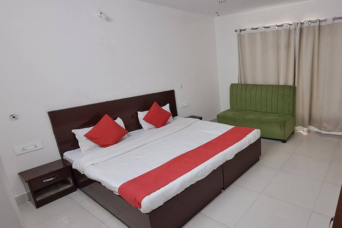 A hotel room with a bed, a green chair, a TV, and curtains.