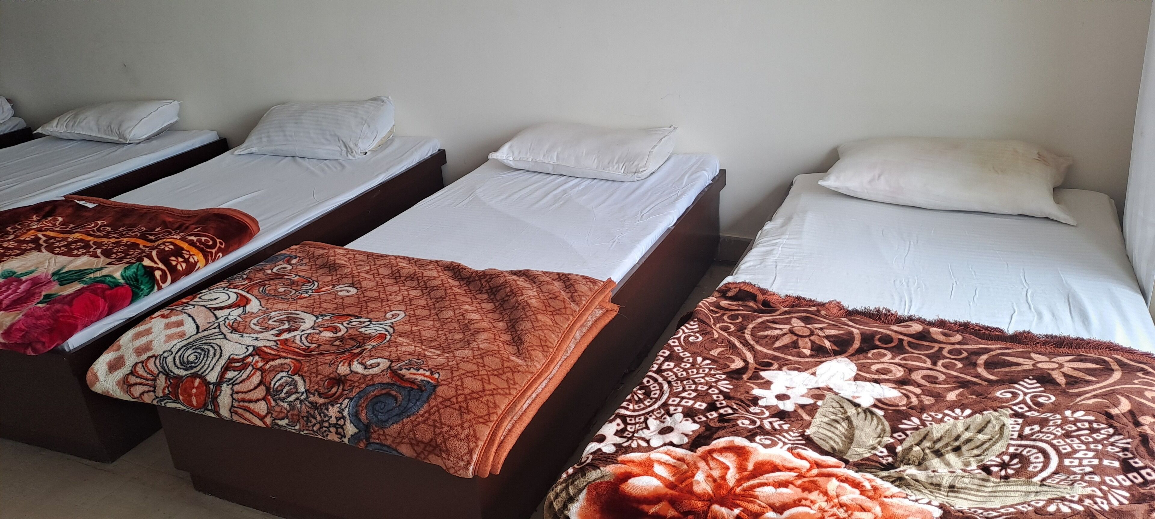Una habitación con cuatro camas, cada una con ropa blanca y mantas de diferentes diseños.