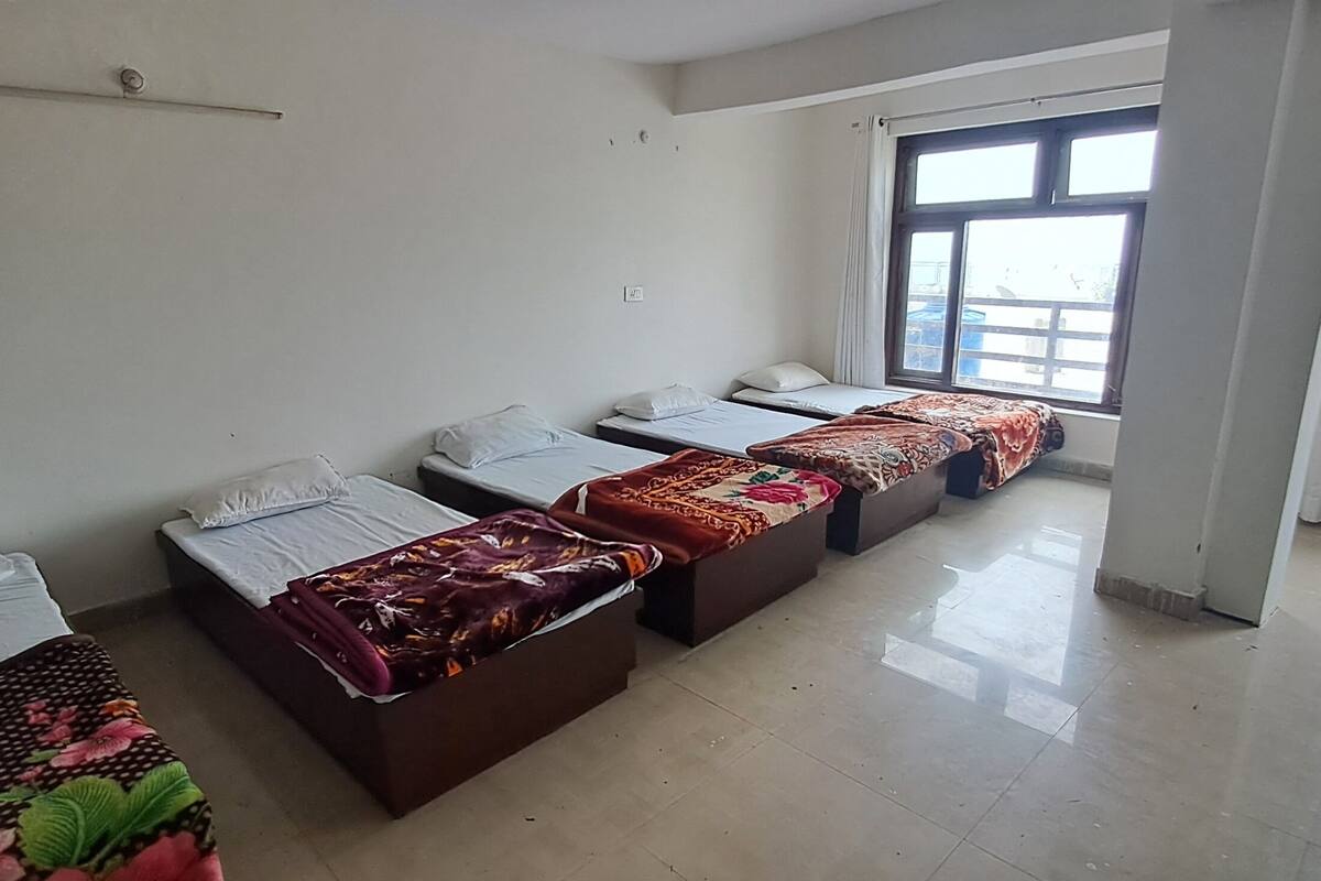 A hotel room with four beds arranged in a row, a large window with curtains, and a tiled floor.
