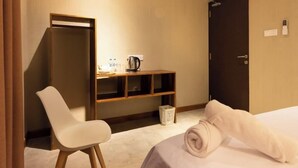 A hotel room with a bed, a chair, a desk with a kettle, and a door. - Kmee Transit hotel & Restaurant (Katunayake)