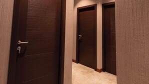 A hallway with three wooden doors, a ceiling light, and a carpeted floor. - Kmee Transit hotel & Restaurant (Katunayake)