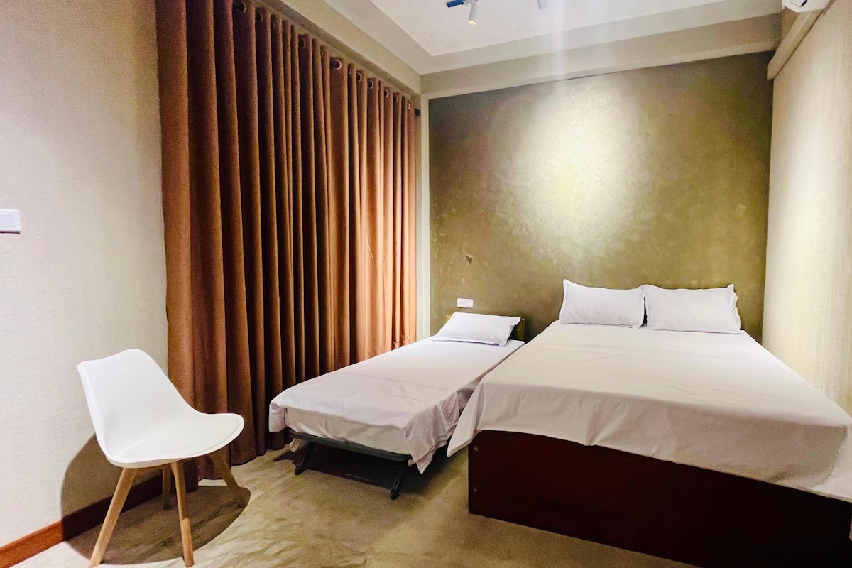 A hotel room with two beds, a chair, and a large window.