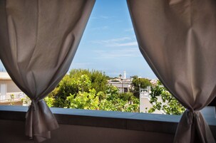 Una finestra con tende annodate in basso, affaccia su una zona residenziale con alberi e palazzi.