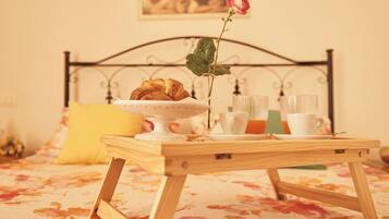 Una bandeja de madera con croissants, un florero con una rosa y una taza de café sobre una cama con colcha estampada.