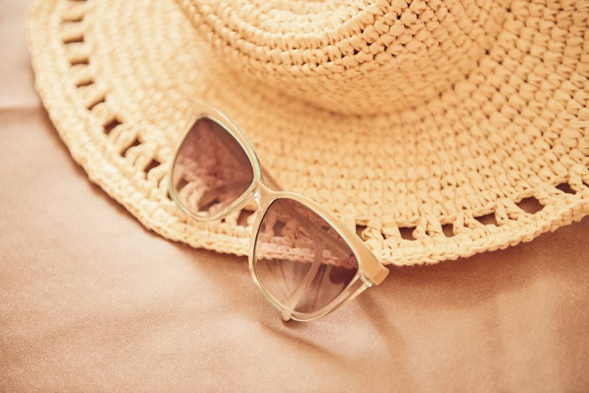 A straw hat and sunglasses on a textured surface.