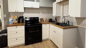 Una cocina compacta con armarios blancos, estufa negra y encimera de madera.