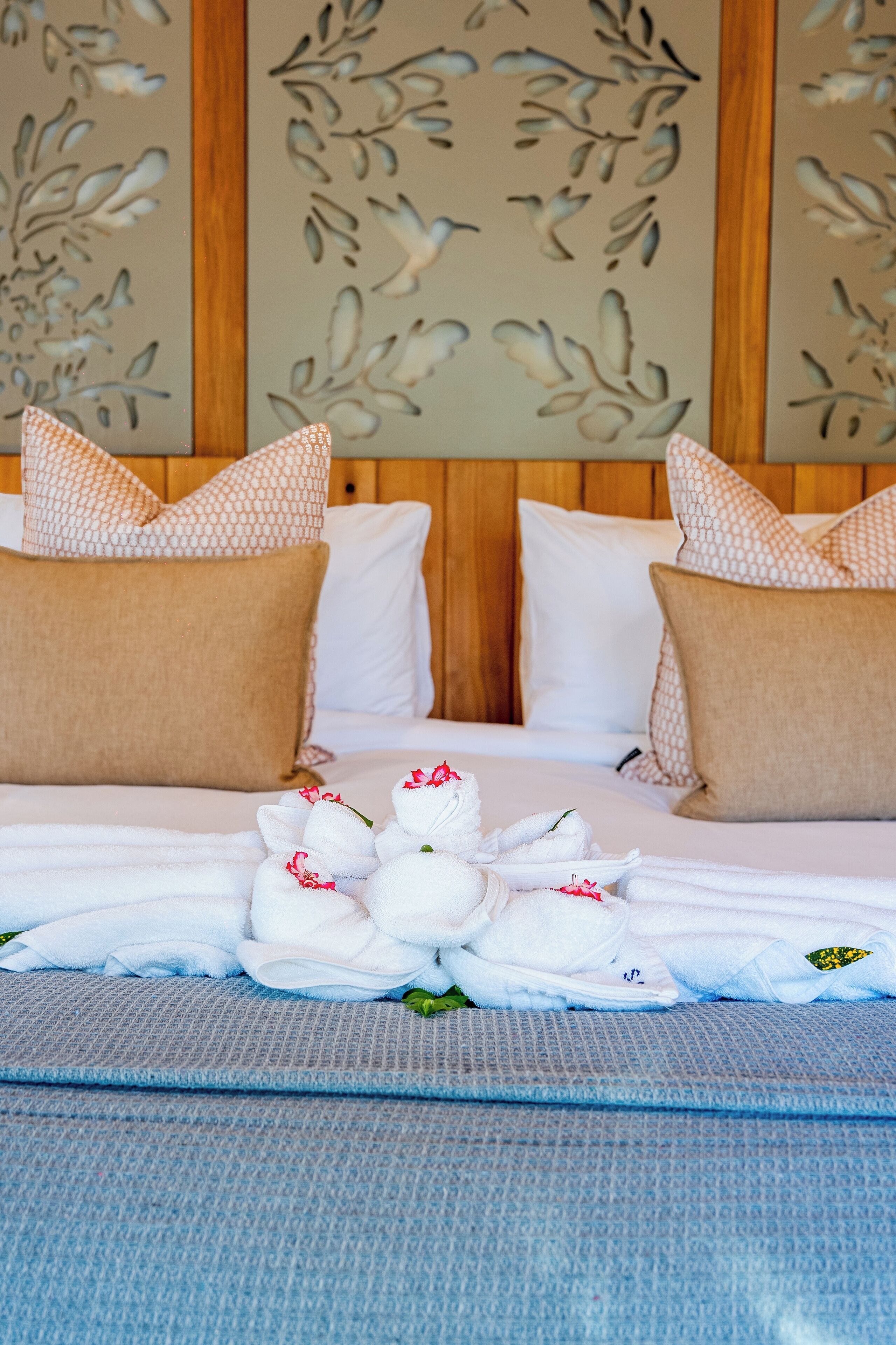 A neatly made bed with white linens, a floral-patterned headboard, and a decorative wall panel in the background.