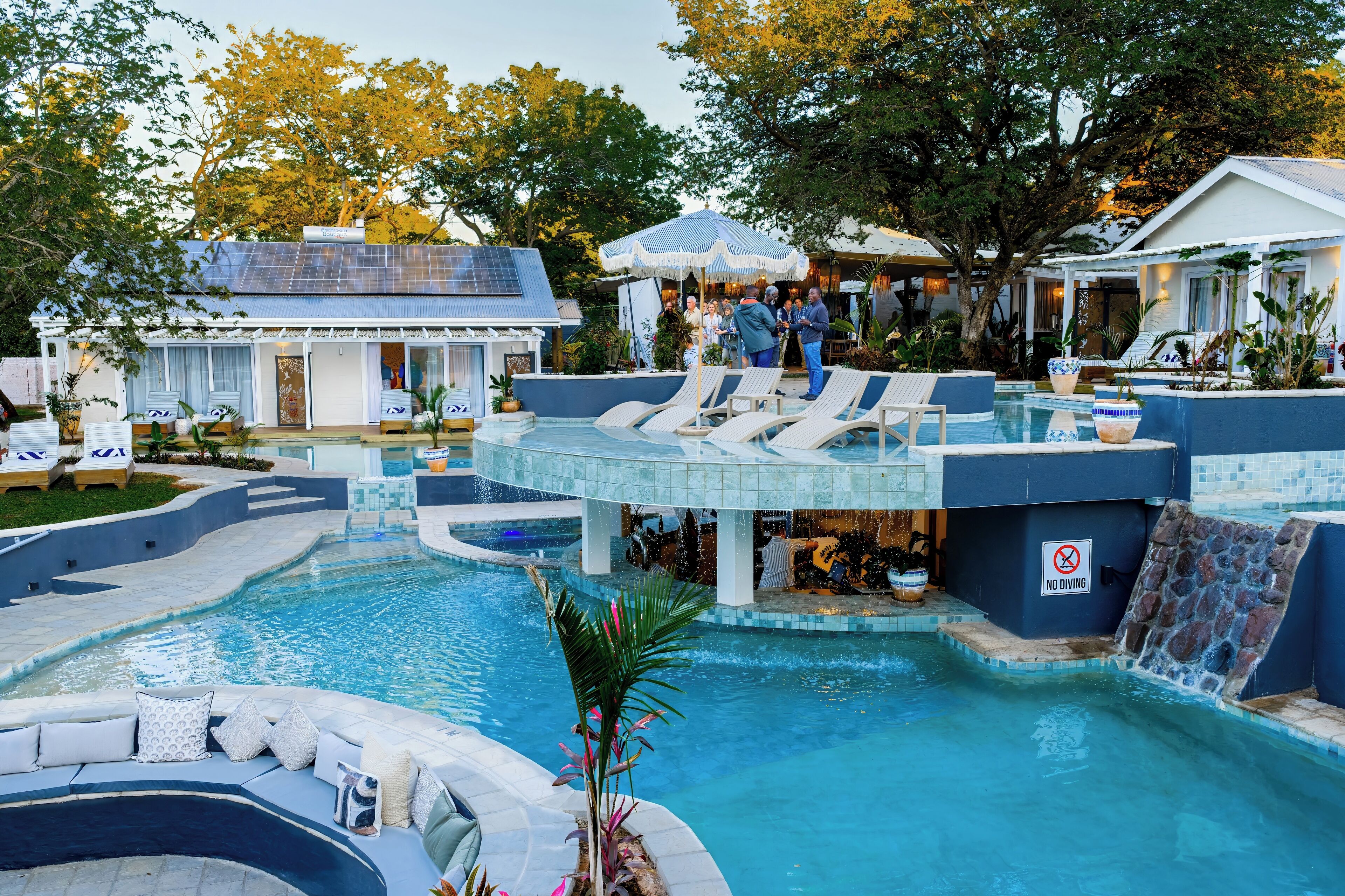 A swimming pool with a waterfall feature, lounge chairs, and a covered area with umbrellas.