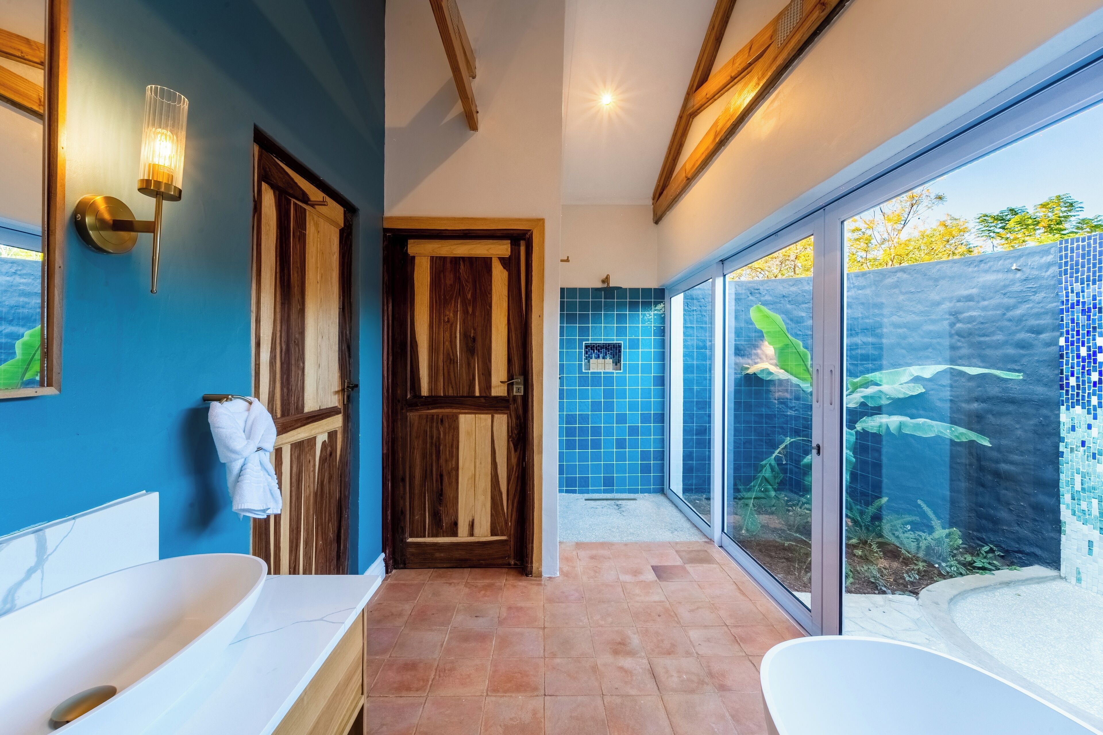 A bathroom with two white sinks, a wooden door, and a blue tiled wall.