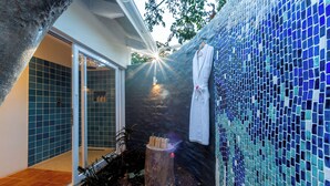 A bathroom with a blue mosaic wall, a wooden bench, and a hanging white towel. - Samanzi (Victoria Falls)
