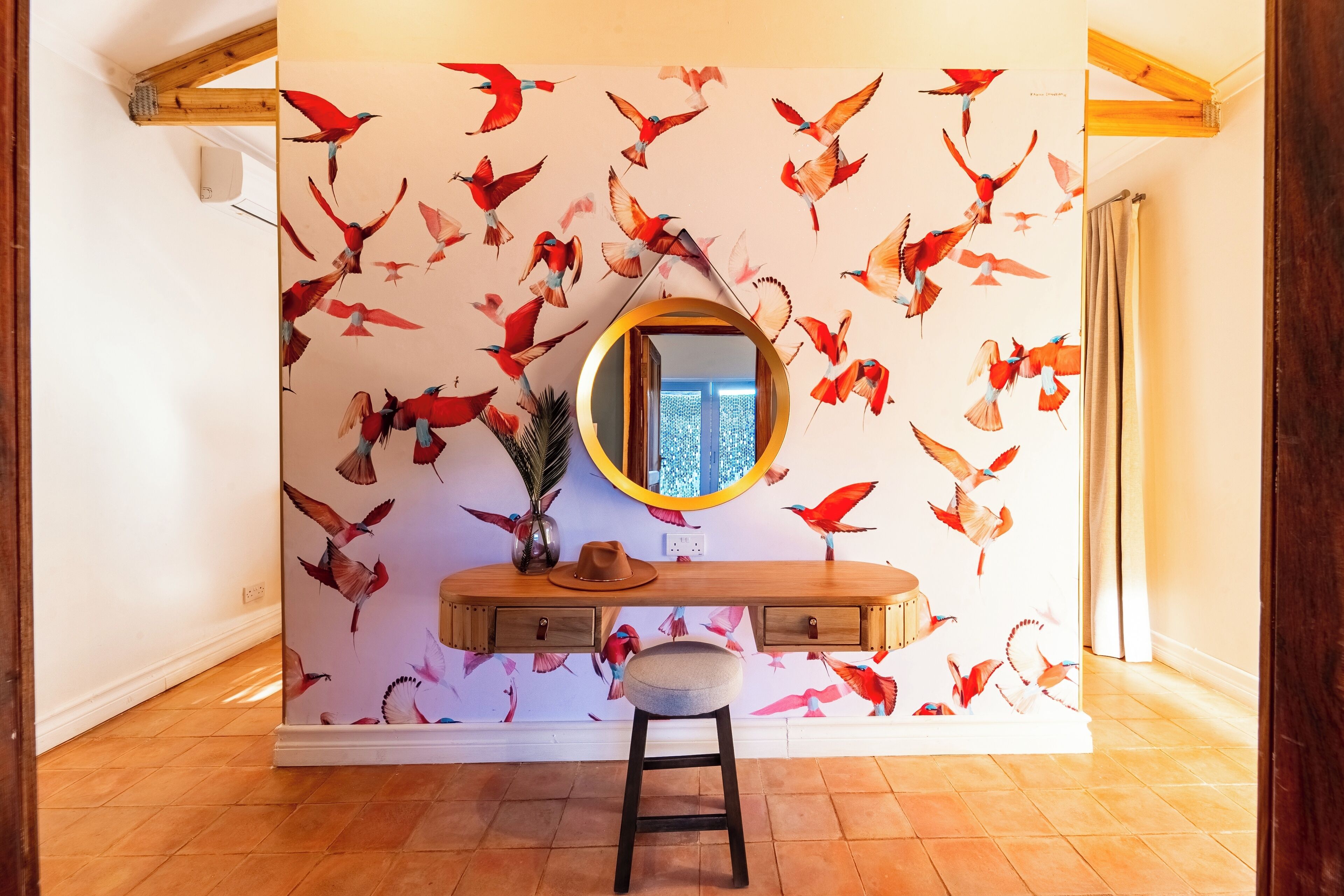 A room with a wooden vanity, a stool, a mirror, and a wall with a bird mural.