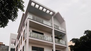 Un edificio residencial de varios pisos con diseño moderno, con balcones en cada planta, entrada protegida por un portón y un camino de acceso.
