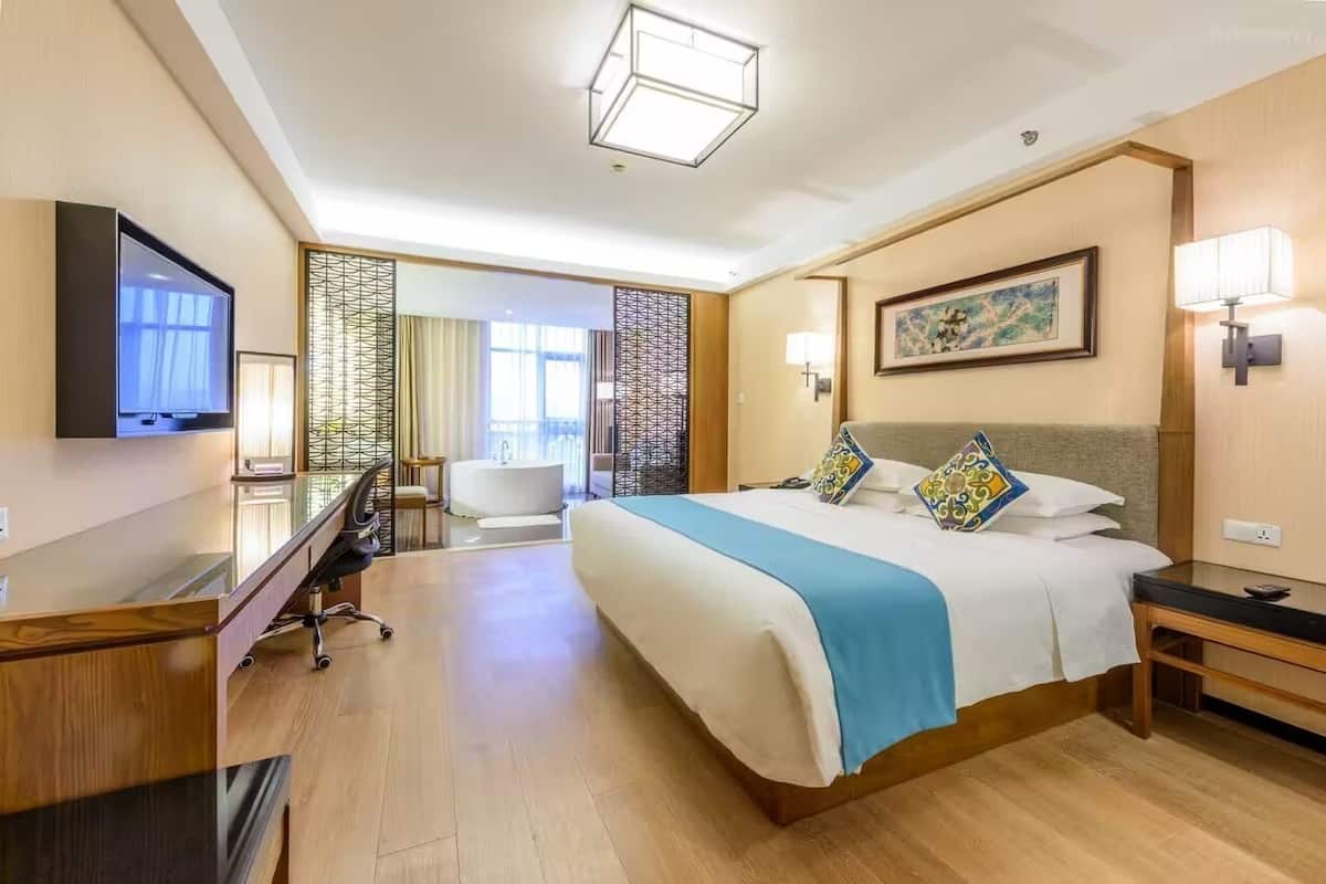 A hotel room with a large bed, a desk, a television, and a bathroom visible through a partition.