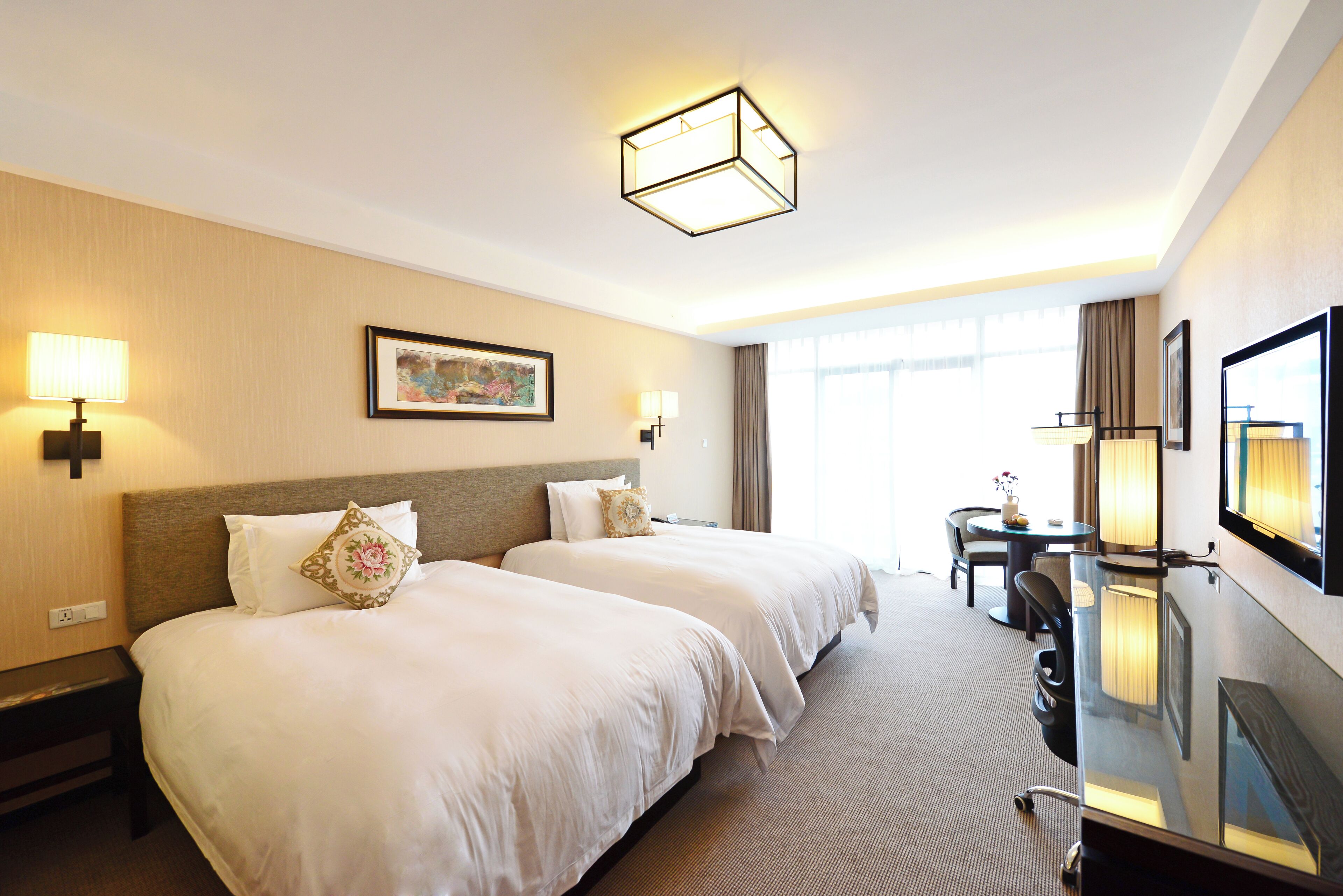 A hotel room with two beds, a desk, a chair, a mirror, and a painting on the wall.