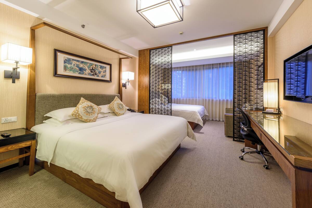 A hotel room with a large bed, a desk, a chair, a TV, and a window with curtains.