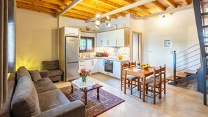 Ein modernes Wohnzimmer mit einer Couch, einem Esstisch mit Stühlen, einer Küche mit Schränken und Geräten sowie einer Treppe.