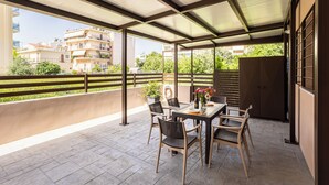 Eine überdachte Terrasse im Freien mit Tisch und Stühlen, einem Blumentopf und Blick auf Gebäude im Hintergrund.