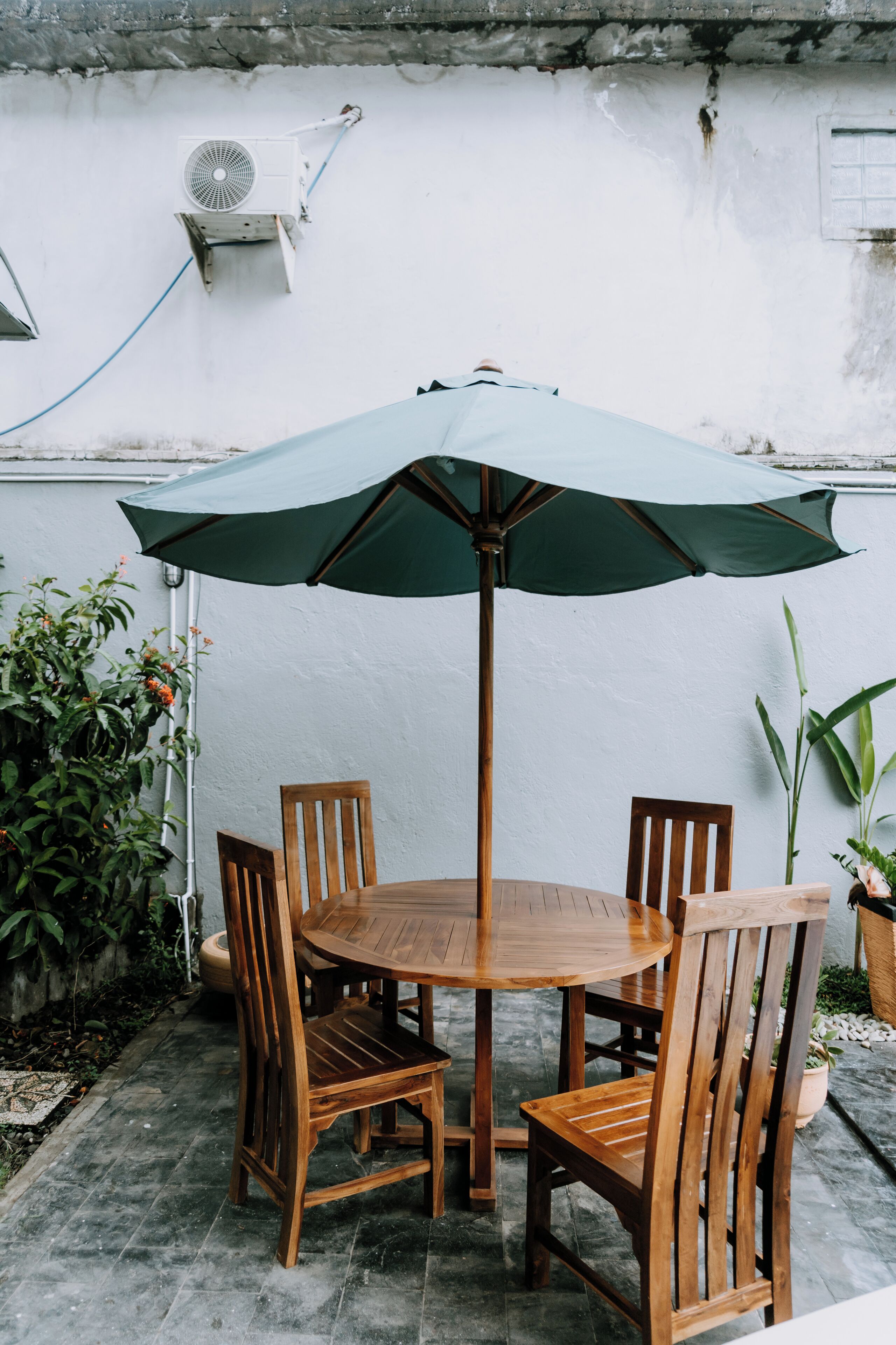 A round wooden table with four chairs and a green umbrella.