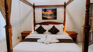 Ein Himmelbett mit einem Gemälde, das einen Sonnenuntergang über dem Meer zeigt, weiße Bettwäsche und ein Paar weiße Bademäntel auf dem Bett.