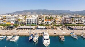 A marina with multiple boats docked, a variety of buildings including a hotel with balconies, and a clear view of the surrounding landscape. - Grand Luxury Apartment Seafront Kalamata (Kalamata)