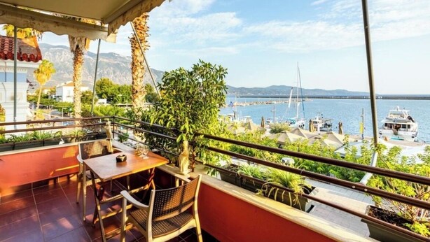 A balcony with a table and chairs, overlooking a marina with boats and a distant mountain range. - Grand Luxury Apartment Seafront Kalamata (Kalamata)