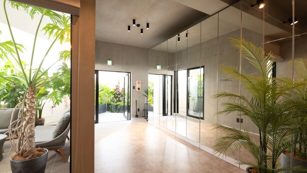 A modern hotel lobby with a glass wall, potted plants, and a seating area. - 730HOTELS (Ishigaki)