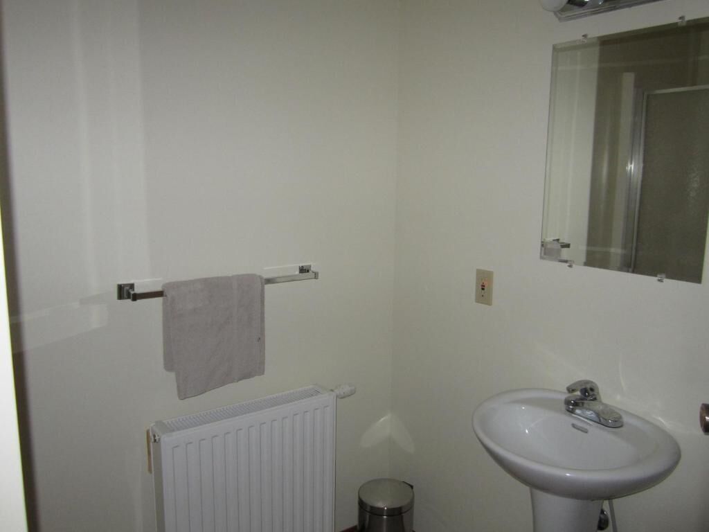 A bathroom with a white radiator, a sink, a mirror, and a towel hanging on a towel rack.