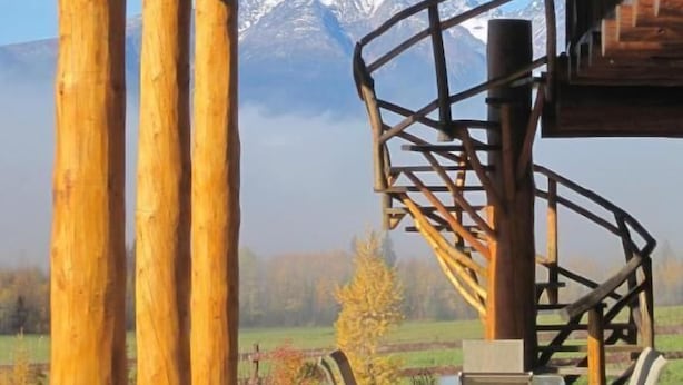 Una estructura de madera con una escalera en espiral, asientos al aire libre y vistas a montañas nevadas.