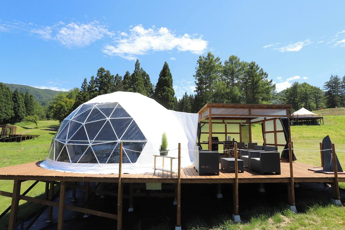 A geodesic dome structure with a wooden deck, outdoor furniture, and a small table with a potted plant.