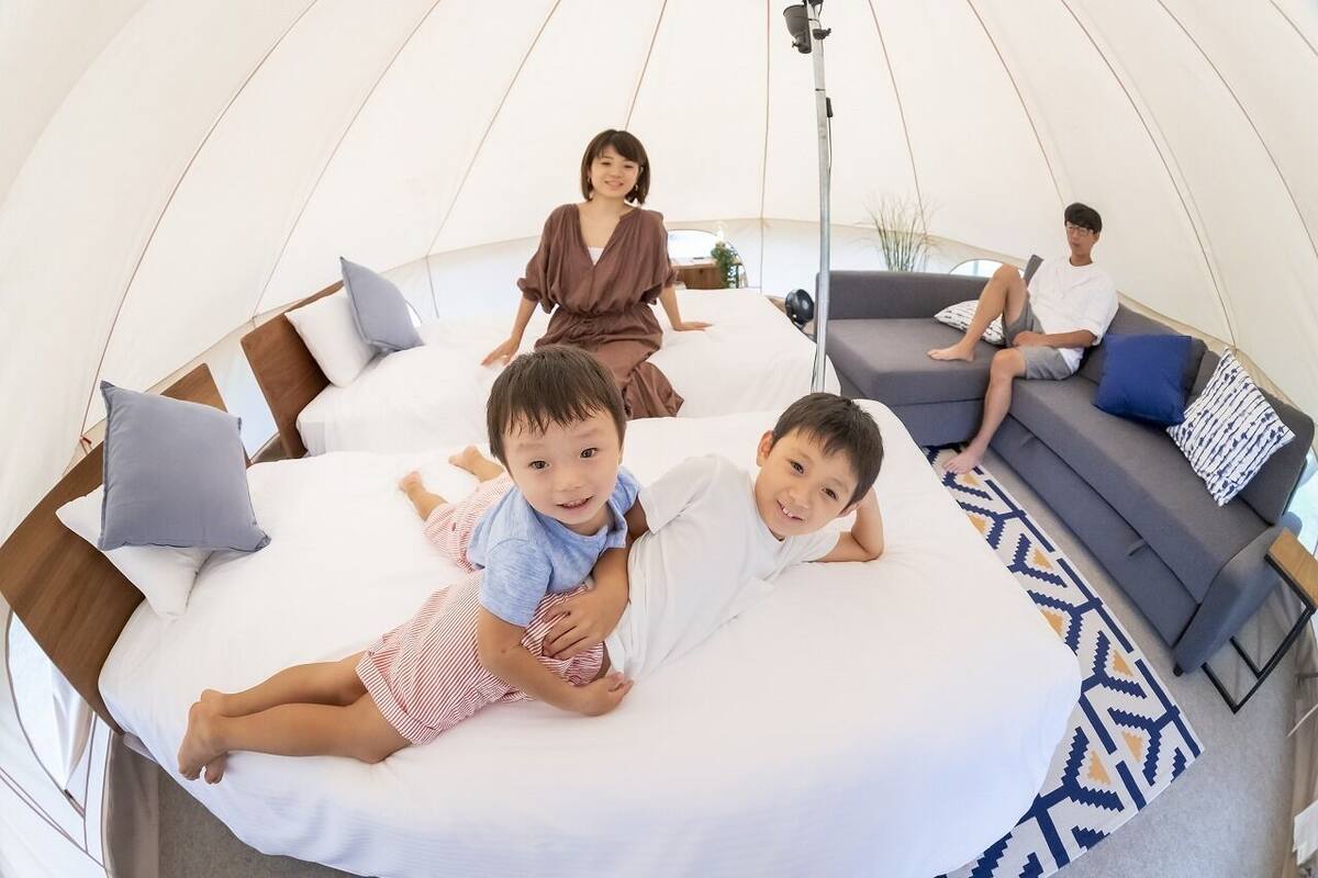 A tent-style room with a bed, a sofa, and a person sitting on the sofa.