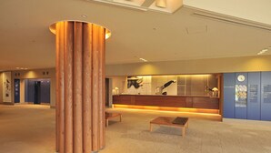 Un moderno vestíbulo de hotel con una columna de madera central, un mostrador de recepción y una zona de estar.
