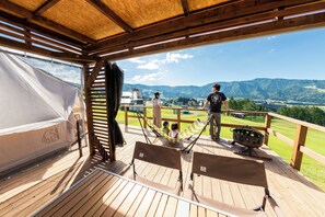 Een houten terras met uitzicht op bergen, een hangmat en een barbecue.