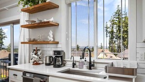 A modern kitchen with white cabinetry, a stainless steel sink, and wooden shelves. - Spectacular Hillside Escape w/ Valley Views, Game Room w/ Pool Table and Foosball, Huge Deck / Patio (Beaverton)