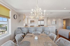 Une cuisine moderne avec des meubles blancs, un îlot central et un coin repas comprenant des chaises en osier et une table en bois.