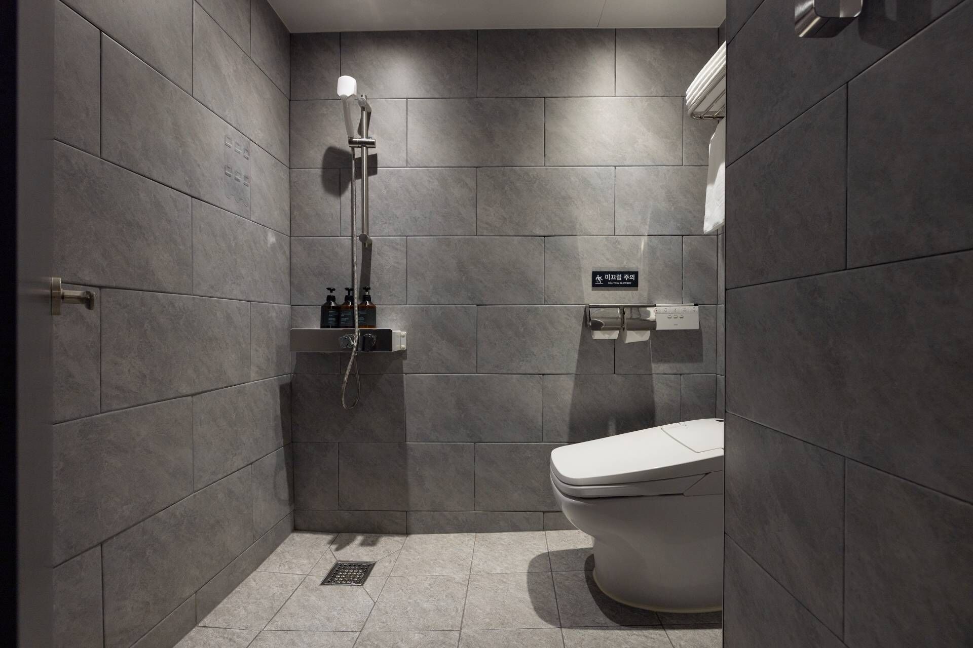 A modern bathroom with a shower, toilet, and a shelf with toiletries.