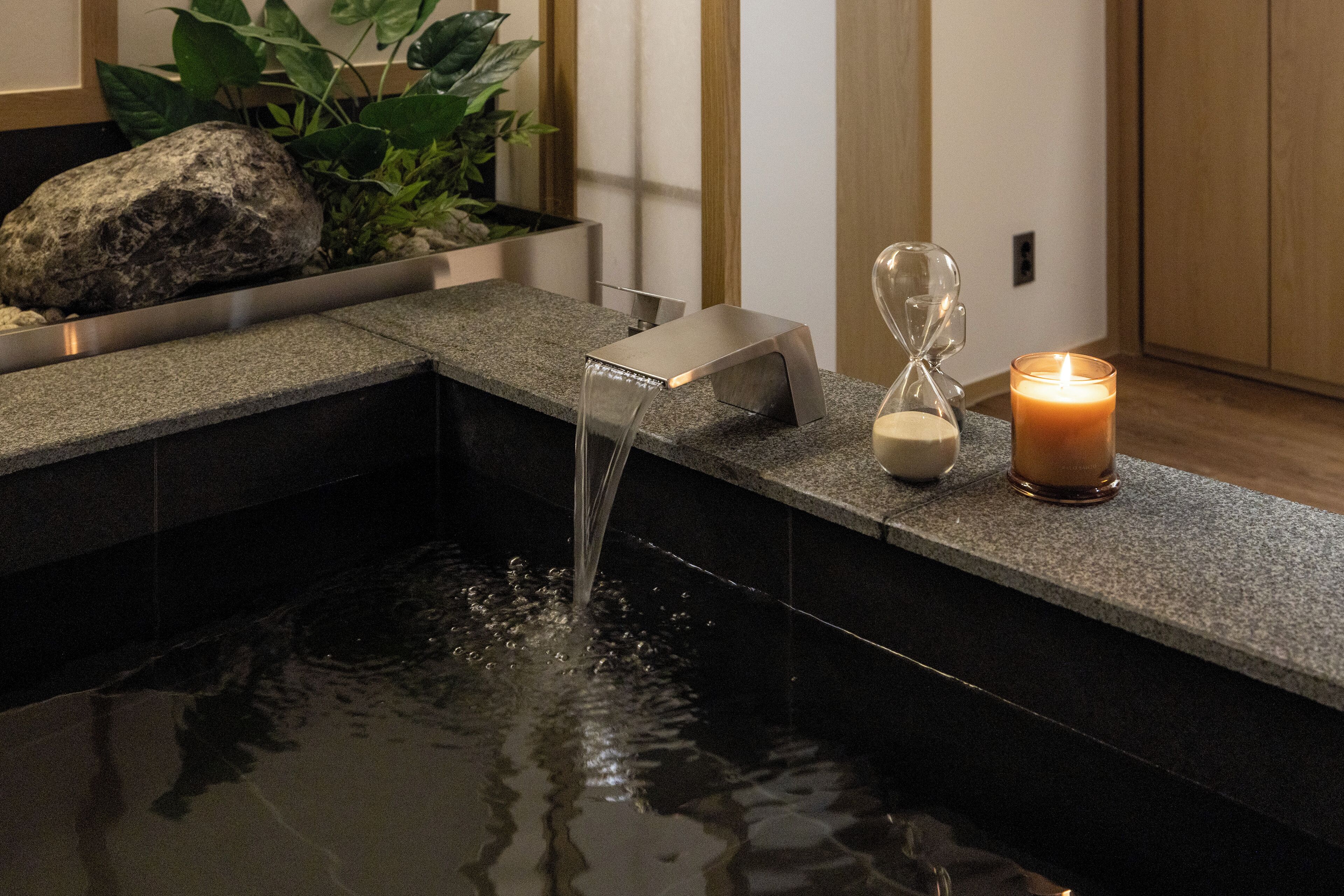 Une salle de bain moderne avec un plan de toilette en pierre, un élément décoratif aquatique et une bougie.