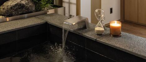 Une salle de bain moderne avec un plan de toilette en pierre, un élément décoratif aquatique et une bougie.