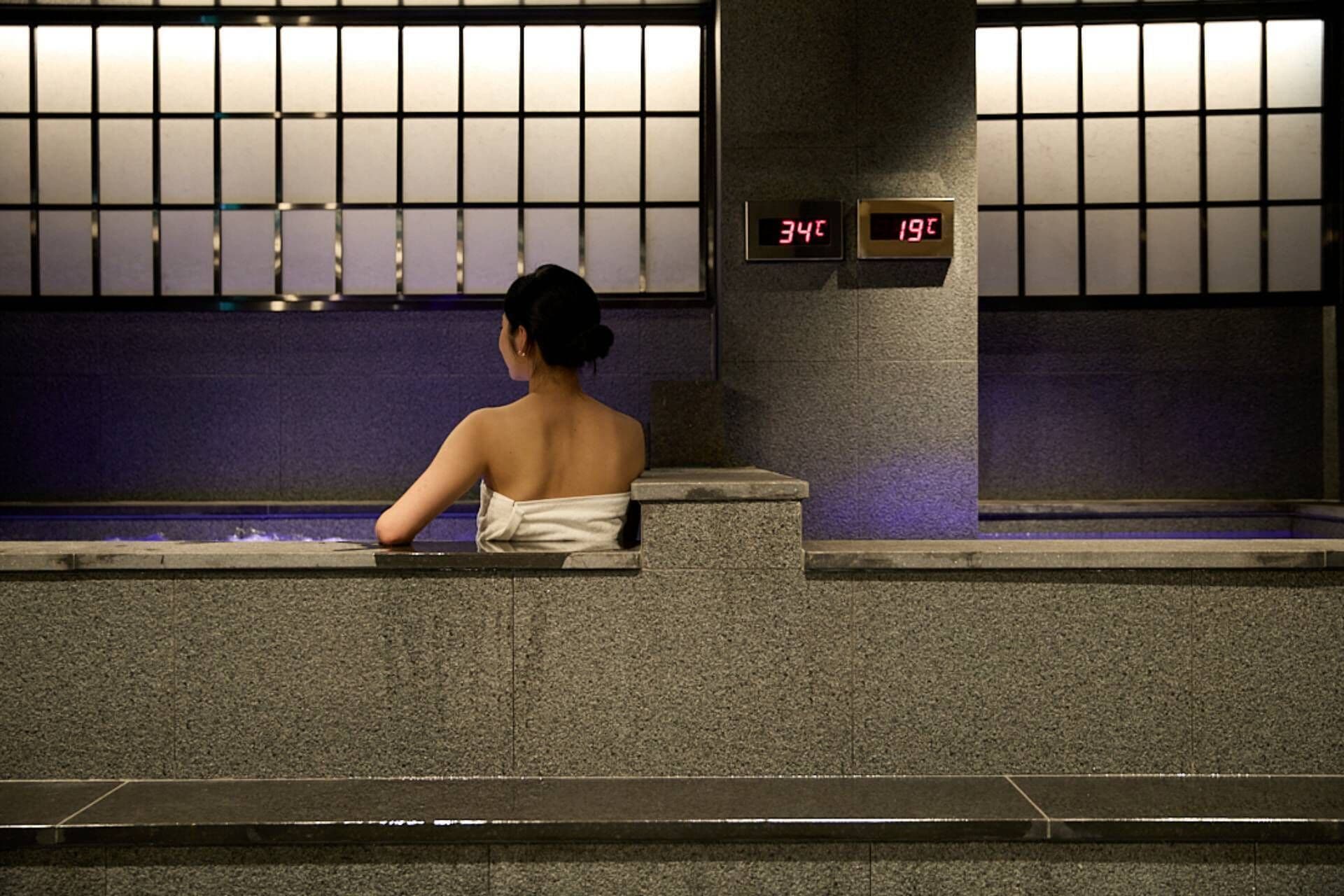 Una persona sentada junto a una piscina, con una pantalla digital que muestra la hora.