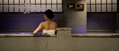 Una persona sentada junto a una piscina, con una pantalla digital que muestra la hora.