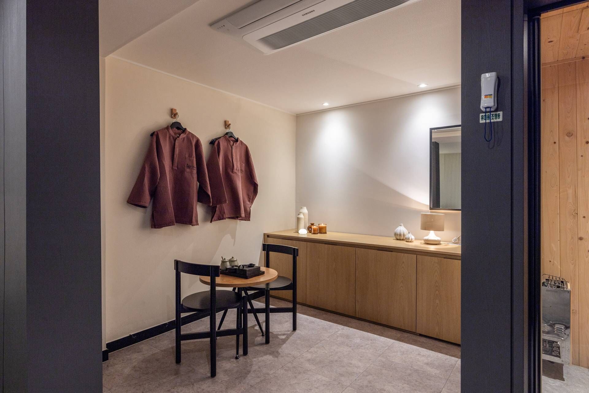 A modern bathroom with a wooden vanity, a mirror, and two hanging robes.