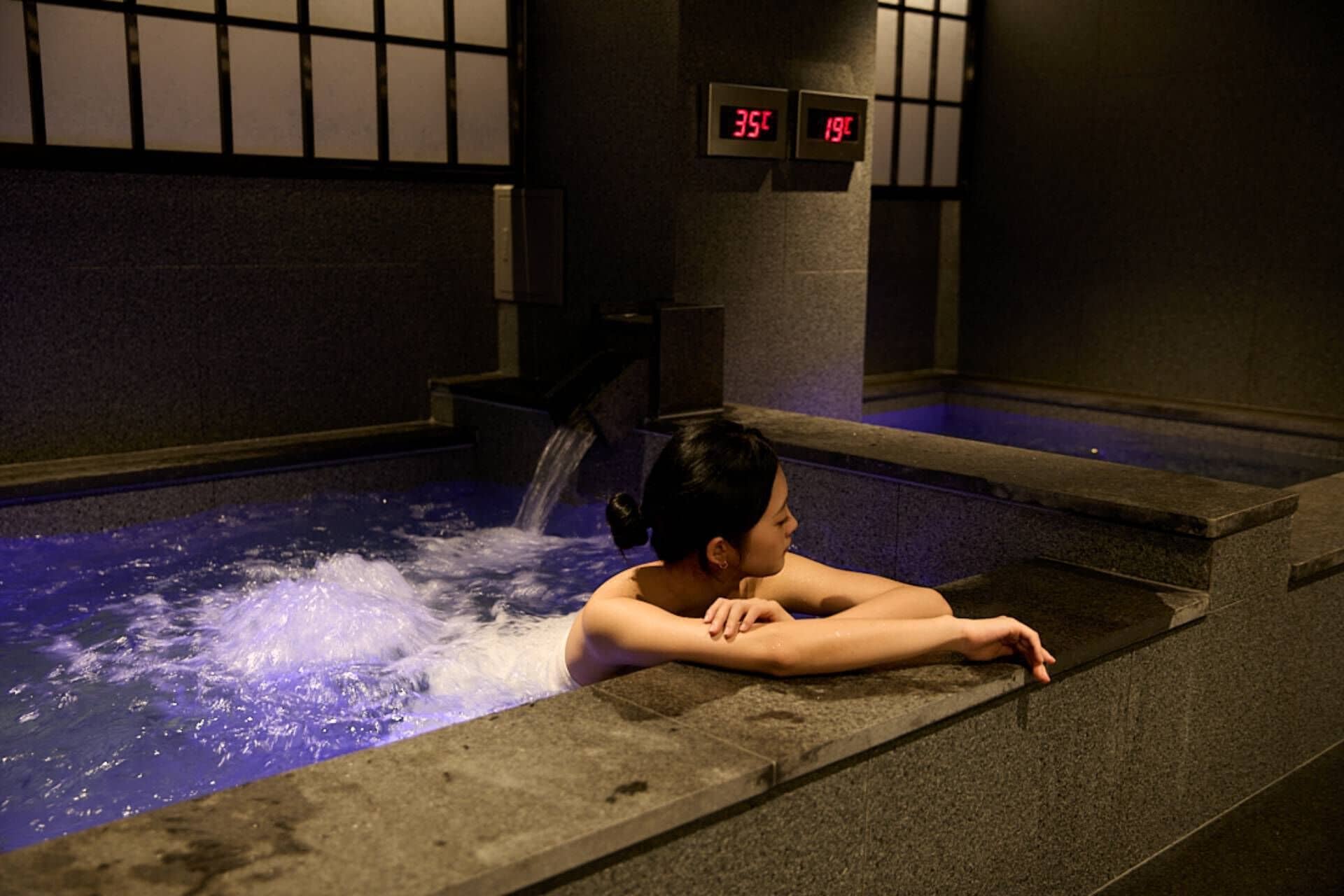 A person relaxing in a hot spring with a digital thermometer displaying 35°C.