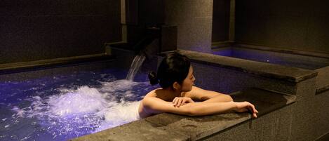 A person relaxing in a hot spring with a digital thermometer displaying 35°C.