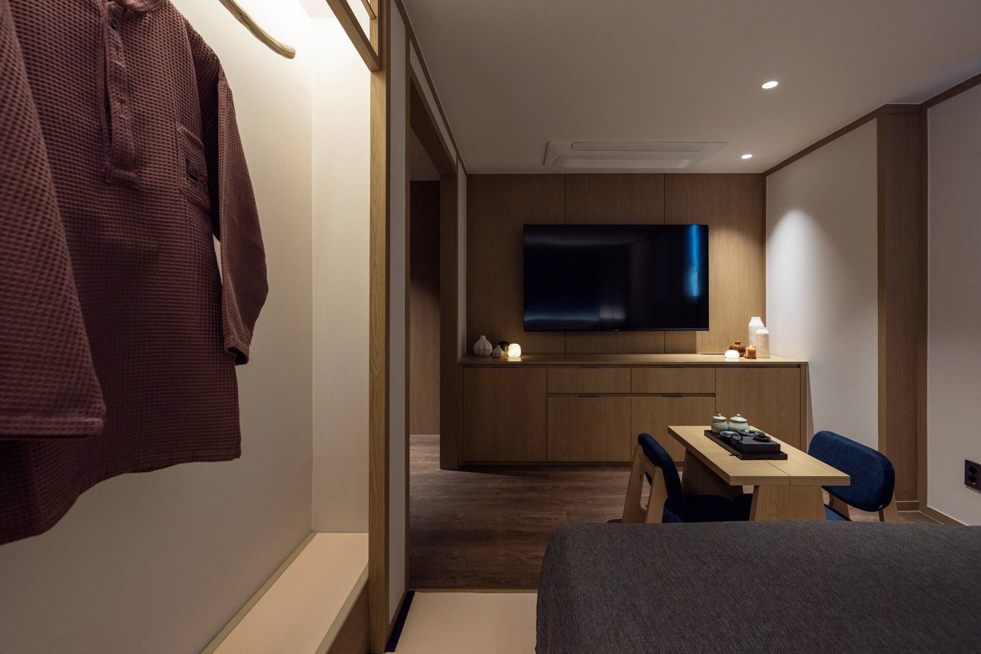 A modern hotel room with a large bed, a desk with a chair, a flat-screen TV mounted on the wall, and a robe hanging on the wall.