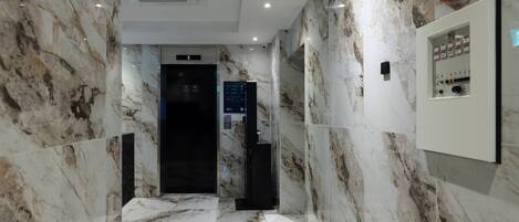 A marble-floored hallway with an elevator and a control panel on the right.